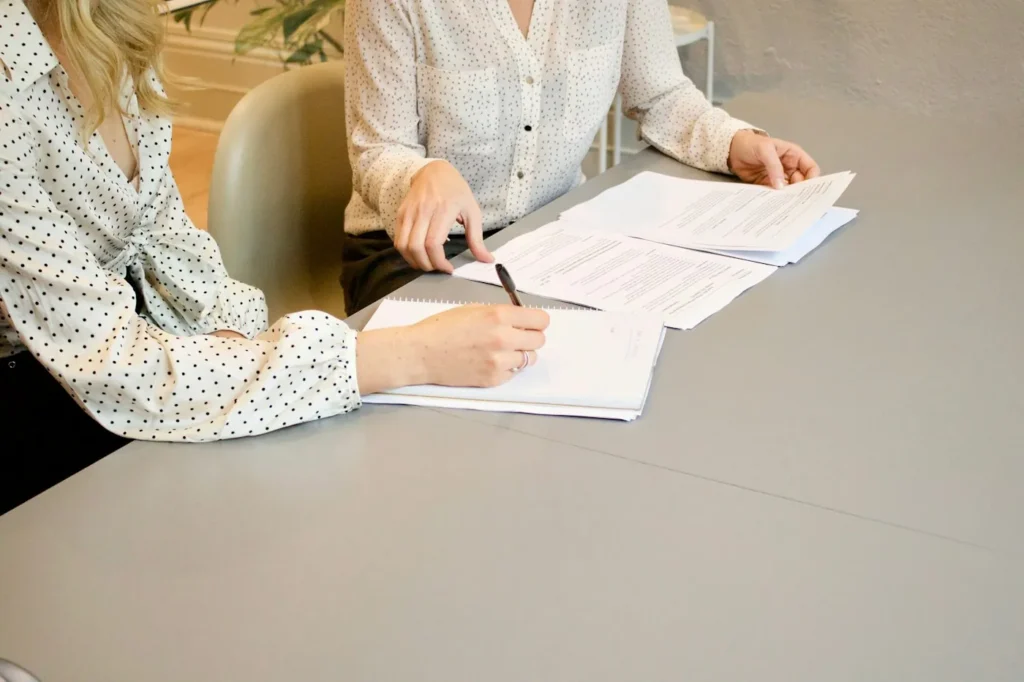 Two women reviewing and signing a business document at a table while forming a company
