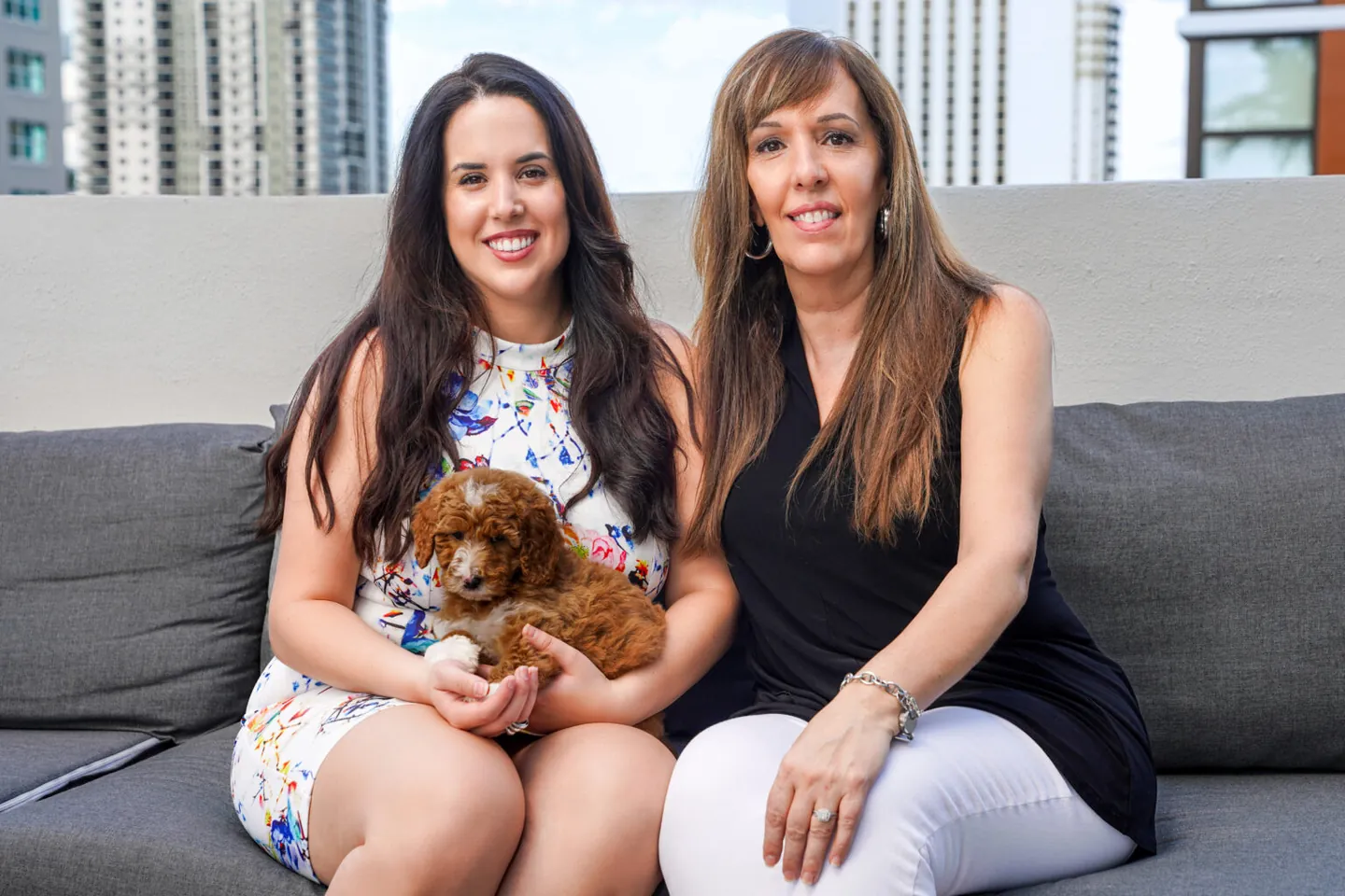 Mena and Rocki Maimone, the mother-daughter team behind Maimone Legal, sitting together with a small dog