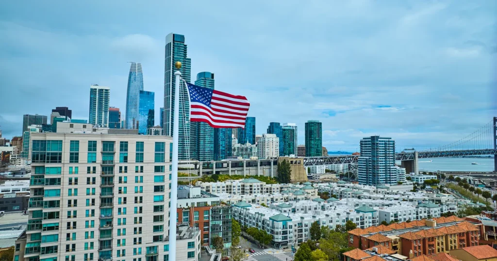 American flag waving above a city skyline, symbolizing the path to a green card through adjustment of status
